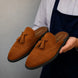 Man holding a pair of Melodiapelle Mendiai Mule shoes in rust tan suede, close-up
