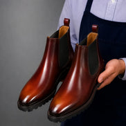 Man holding a pair of Melodiapelle Mentor Classic Chelsea Boots in burnt ombre leather, close-up