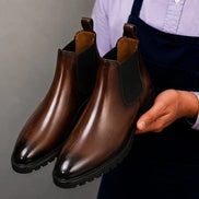 Man holding a pair of Melodiapelle Mentor Classic Chelsea Boots in dark brown leather, close-up