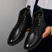 Man holding a pair of Melodiapelle Meridian Combat Boots in black leather, close-up