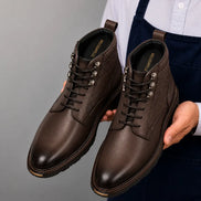 Man holding a pair of Melodiapelle Meridian Combat Boots in dark brown leather, close-up