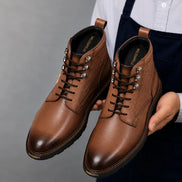 Man holding a pair of Melodiapelle Meridian Combat Boots in tan leather, close-up