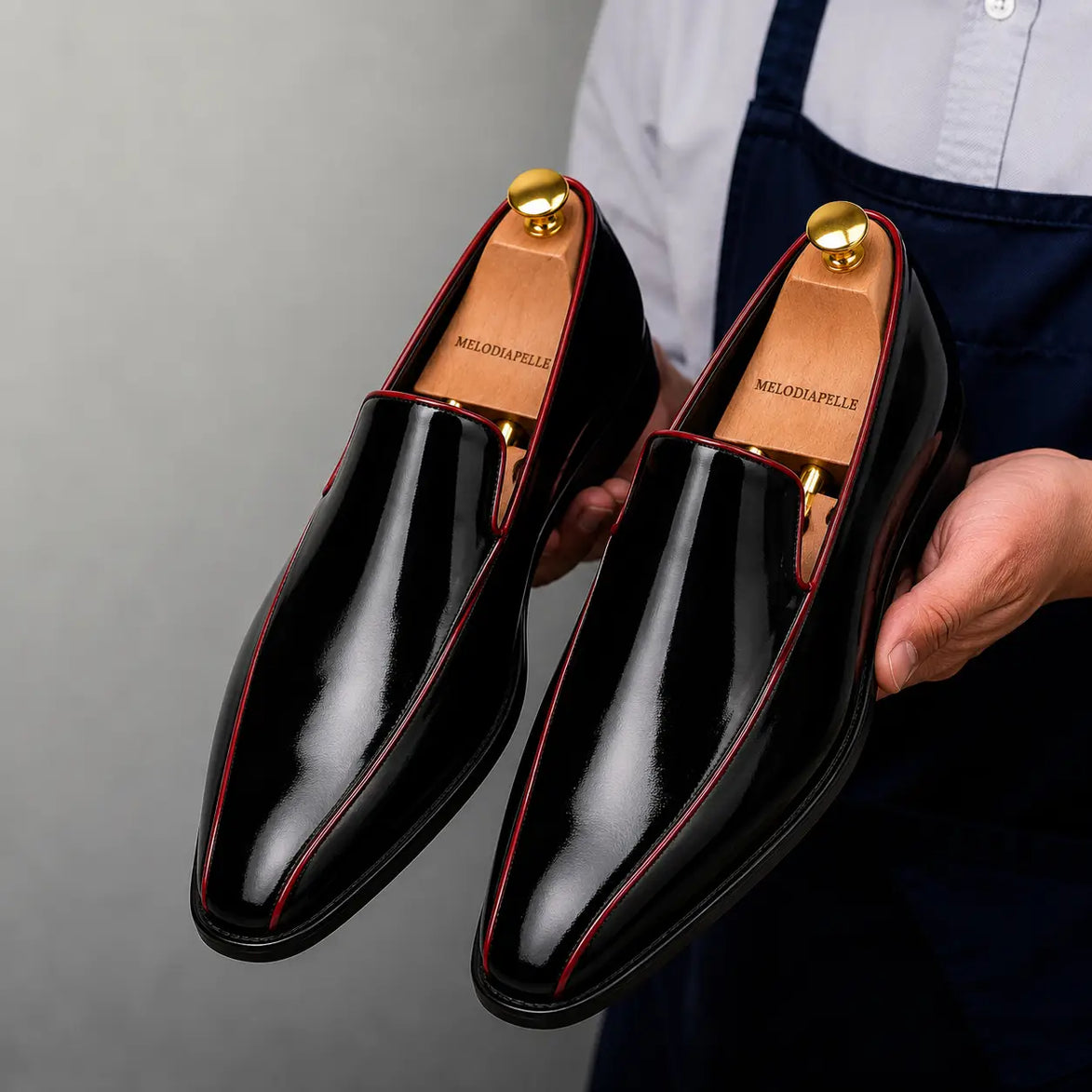 Man holding a pair of Melodiapelle Merlot Dress Loafer shoes in nero black leather with red piping, close-up