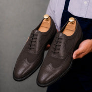 Man holding a pair of Melodiapelle Meta Semi-Brogue Oxford shoes in dark brown leather, close-up