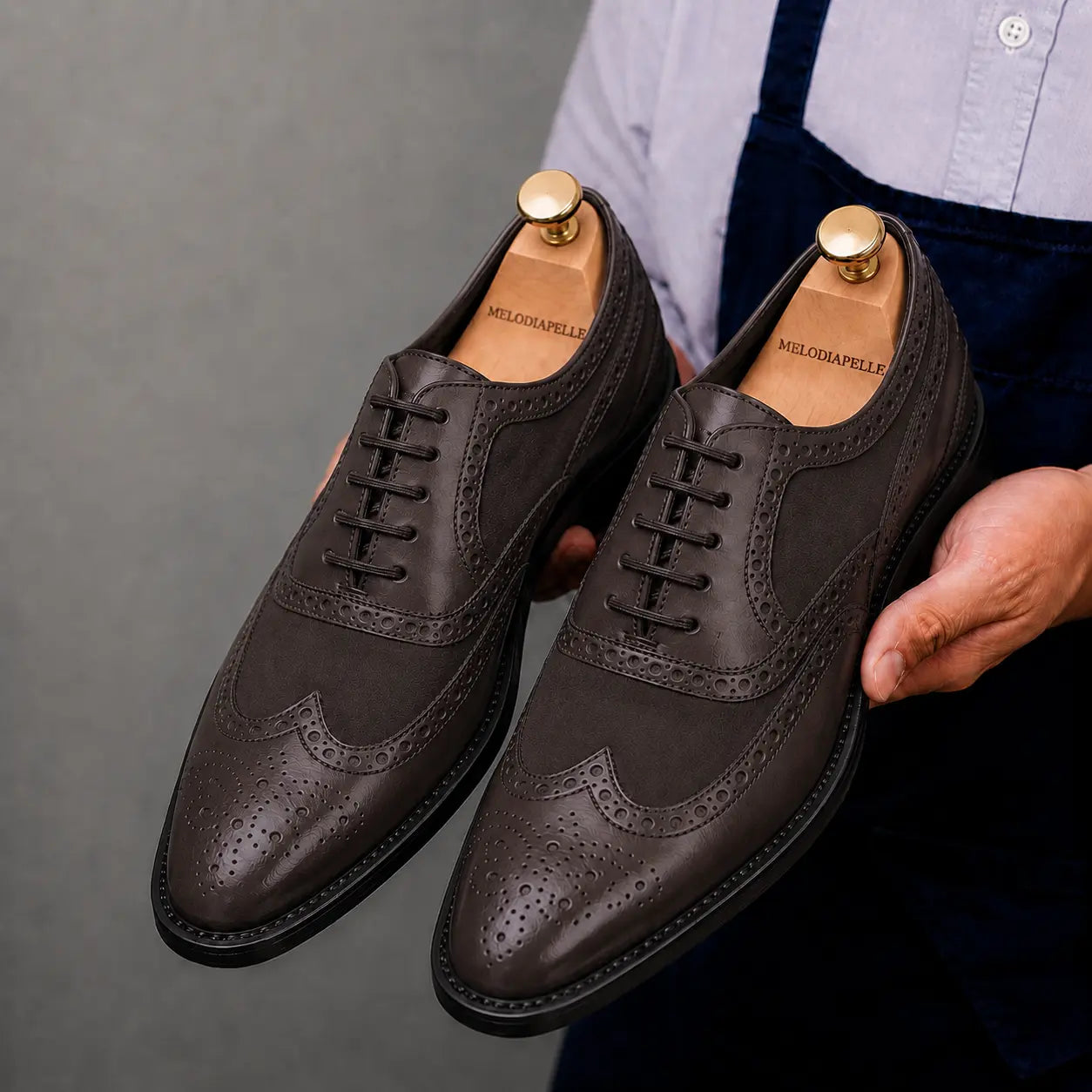Man holding a pair of Melodiapelle Meta Semi-Brogue Oxford shoes in dark brown leather, close-up