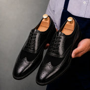 Man holding a pair of Melodiapelle Meta Semi-Brogue Oxford shoes in nero black leather, close-up