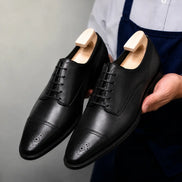 Man holding a pair of Melodiapelle Meta Wholecut Oxford shoes in black leather, close-up