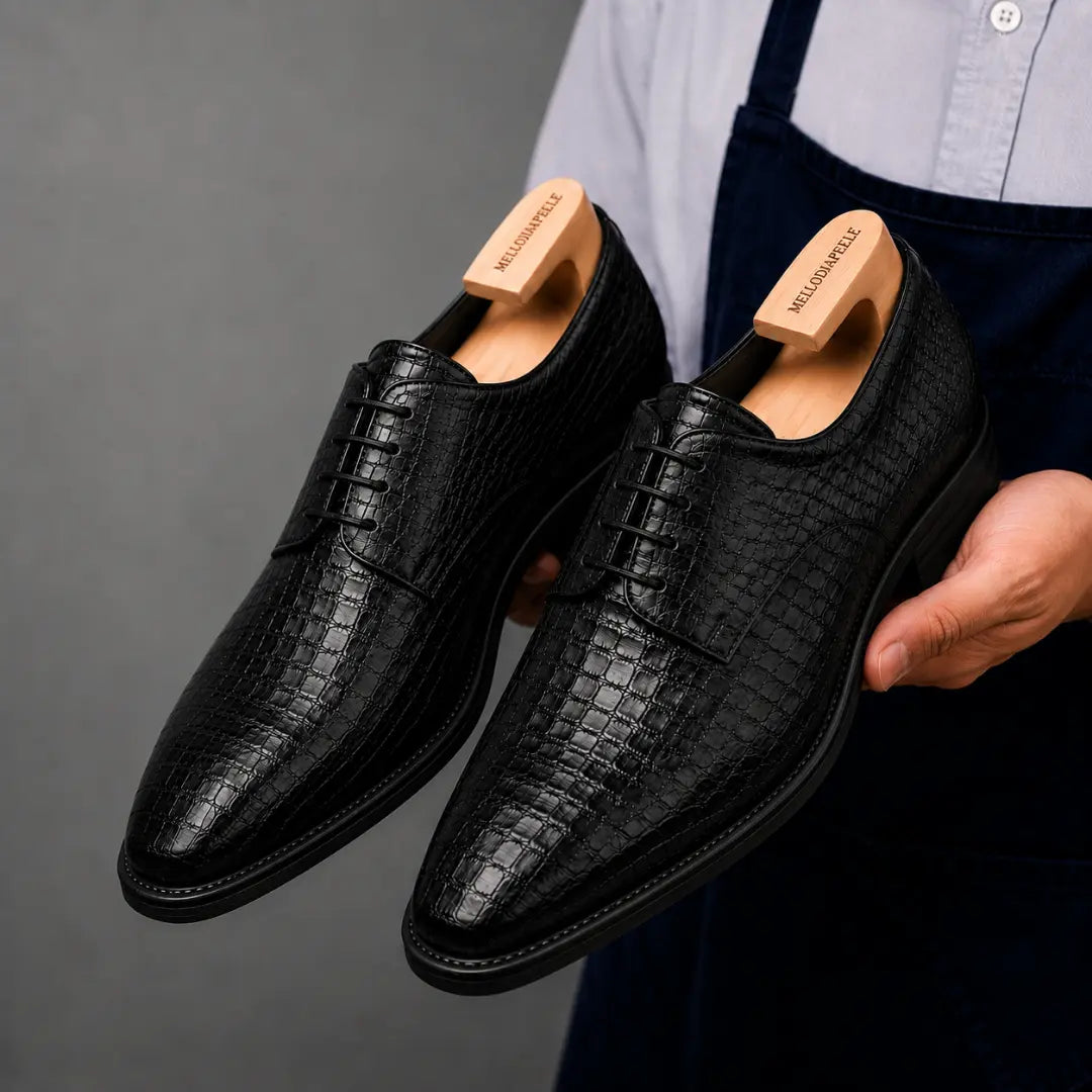 Man holding a pair of Melodiapelle Meta Wholecut Oxford shoes in black croc-embossed leather, close-up