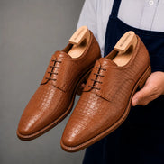 Man holding a pair of Melodiapelle Meta Wholecut Oxford shoes in tan croc-embossed leather, close-up