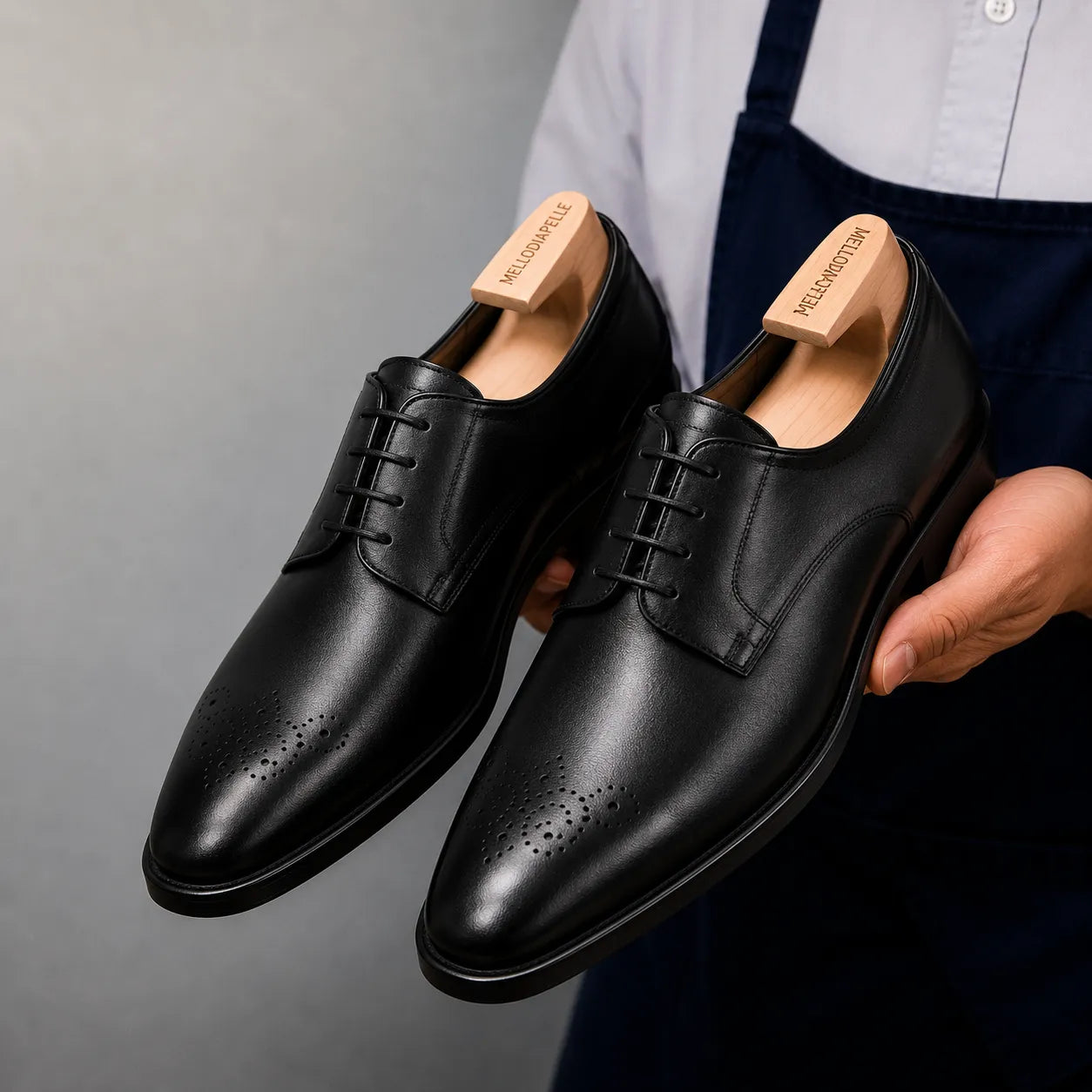 Man holding a pair of Melodiapelle Meta Wholecut Oxford shoes in nero black leather, close-up