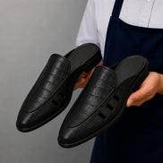 Man holding a pair of Melodiapelle Miami Mule shoes in black leather, close-up