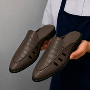 Man holding a pair of Melodiapelle Miami Mule shoes in dark brown leather, close-up