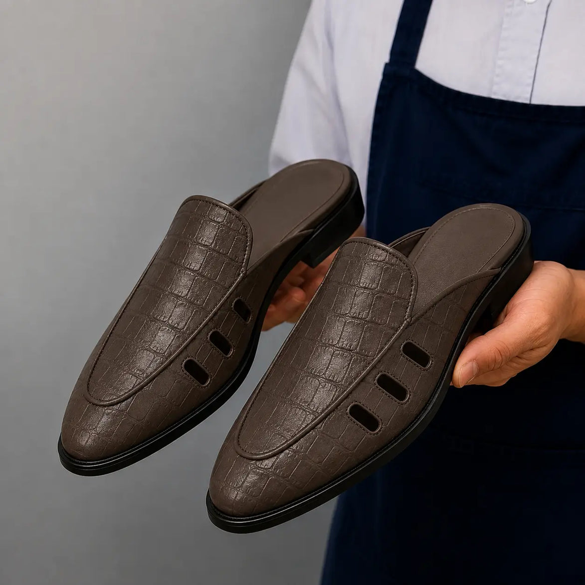 Man holding a pair of Melodiapelle Miami Mule shoes in dark brown leather, close-up