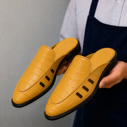 Man holding a pair of Melodiapelle Miami Mule shoes in mustard yellow leather, close-up