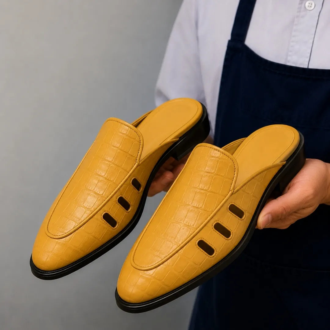 Man holding a pair of Melodiapelle Miami Mule shoes in mustard yellow leather, close-up