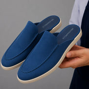 Man holding a pair of Melodiapelle Michelle Mule shoes in royal blue suede, close-up