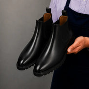 Man holding a pair of Melodiapelle Michigan Chelsea Boots in black leather, close-up