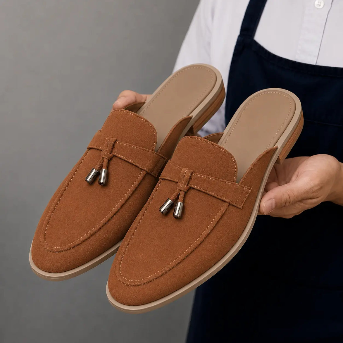 Man holding a pair of Melodiapelle Micol Mule shoes in rust tan suede, close-up