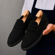 Man holding a pair of Melodiapelle Midland Loafer shoes in black suede, close-up