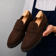 Man holding a pair of Melodiapelle Midland Loafer shoes in dark brown suede, close-up