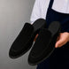 Man holding a pair of Melodiapelle Mila Mule shoes in black suede, close-up