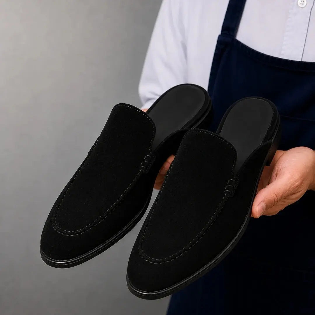 Man holding a pair of Melodiapelle Mila Mule shoes in black suede, close-up
