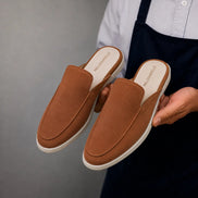 Man holding a pair of Melodiapelle Mila Mule shoes in rust tan suede, close-up