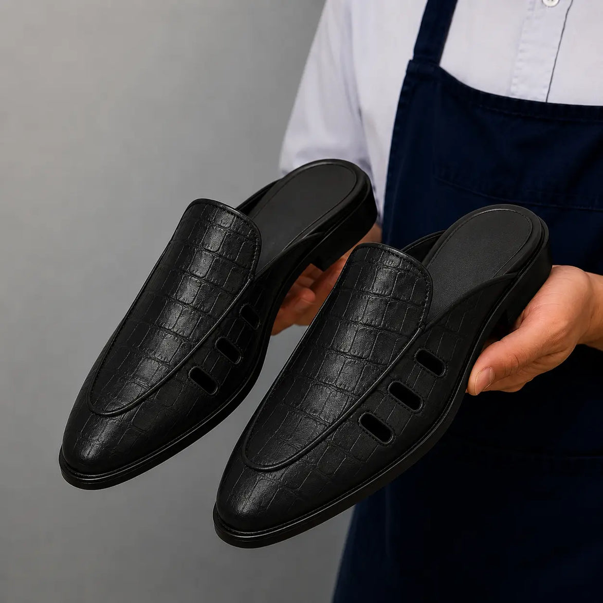 Man holding a pair of Melodiapelle Milan Mule shoes in black embossed leather, close-up
