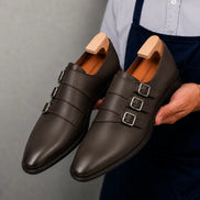 Man holding a pair of Melodiapelle Milan Triple Monk Strap Loafer shoes in brown leather, close-up