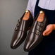 Man holding a pair of Melodiapelle Milan Triple Monk Strap Loafer shoes in brown leather, close-up