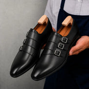 Man holding a pair of Melodiapelle Milan Triple Monk Strap Loafer shoes in nero black leather, close-up