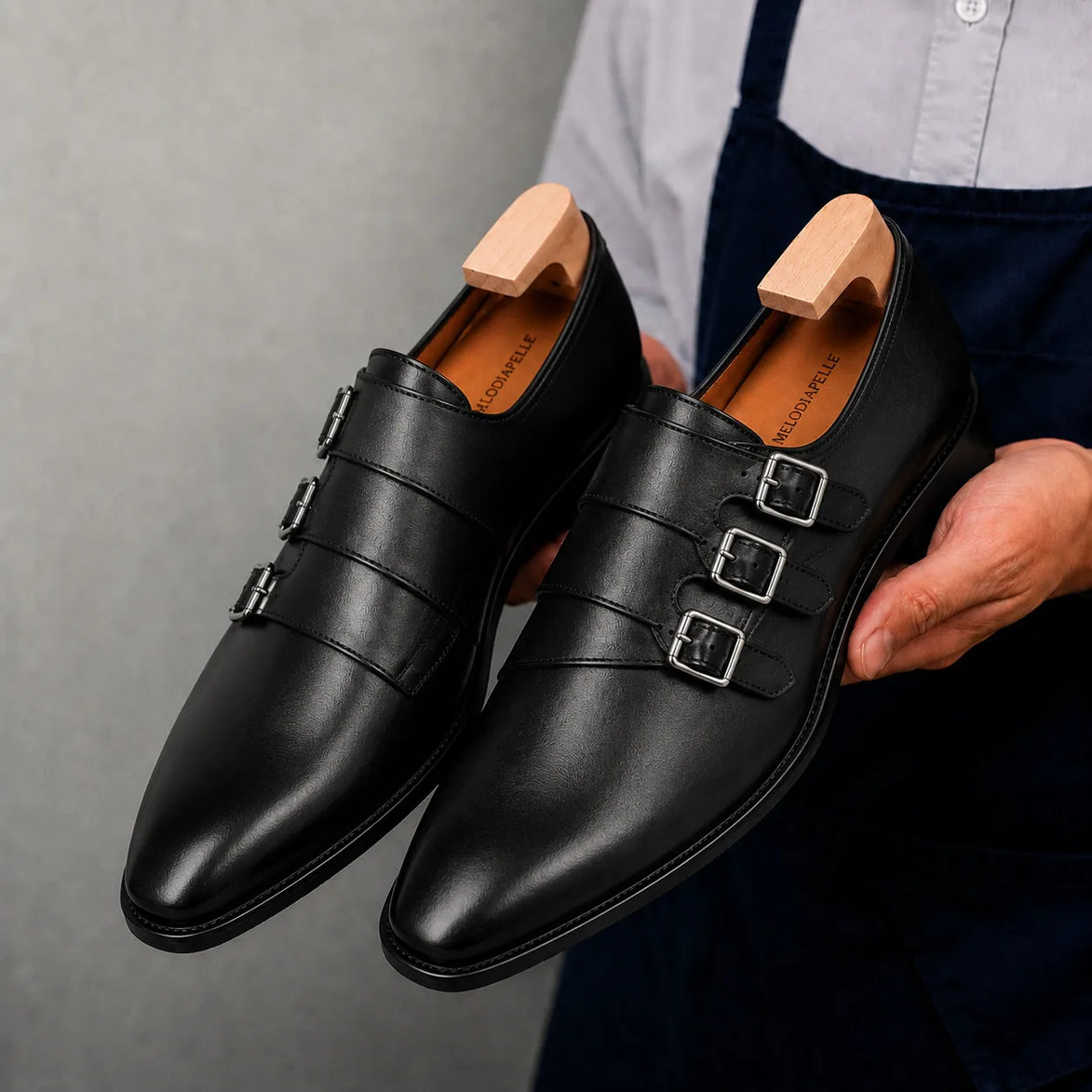 Man holding a pair of Melodiapelle Milan Triple Monk Strap Loafer shoes in nero black leather, close-up