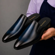 Man holding a pair of Melodiapelle Millburn Mules in black leather, close-up