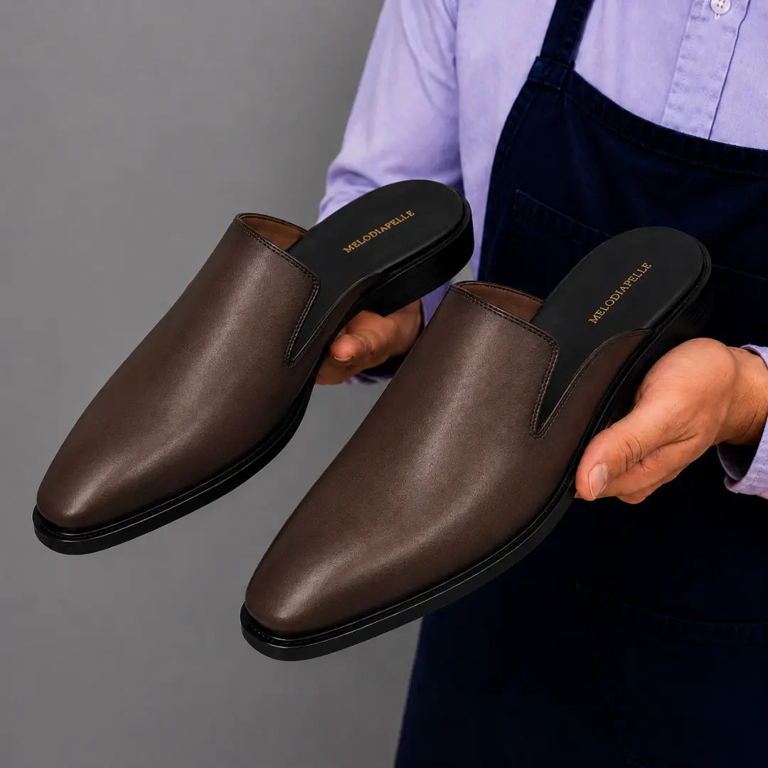 Man holding a pair of Melodiapelle Millburn Mules in dark brown leather, close-up