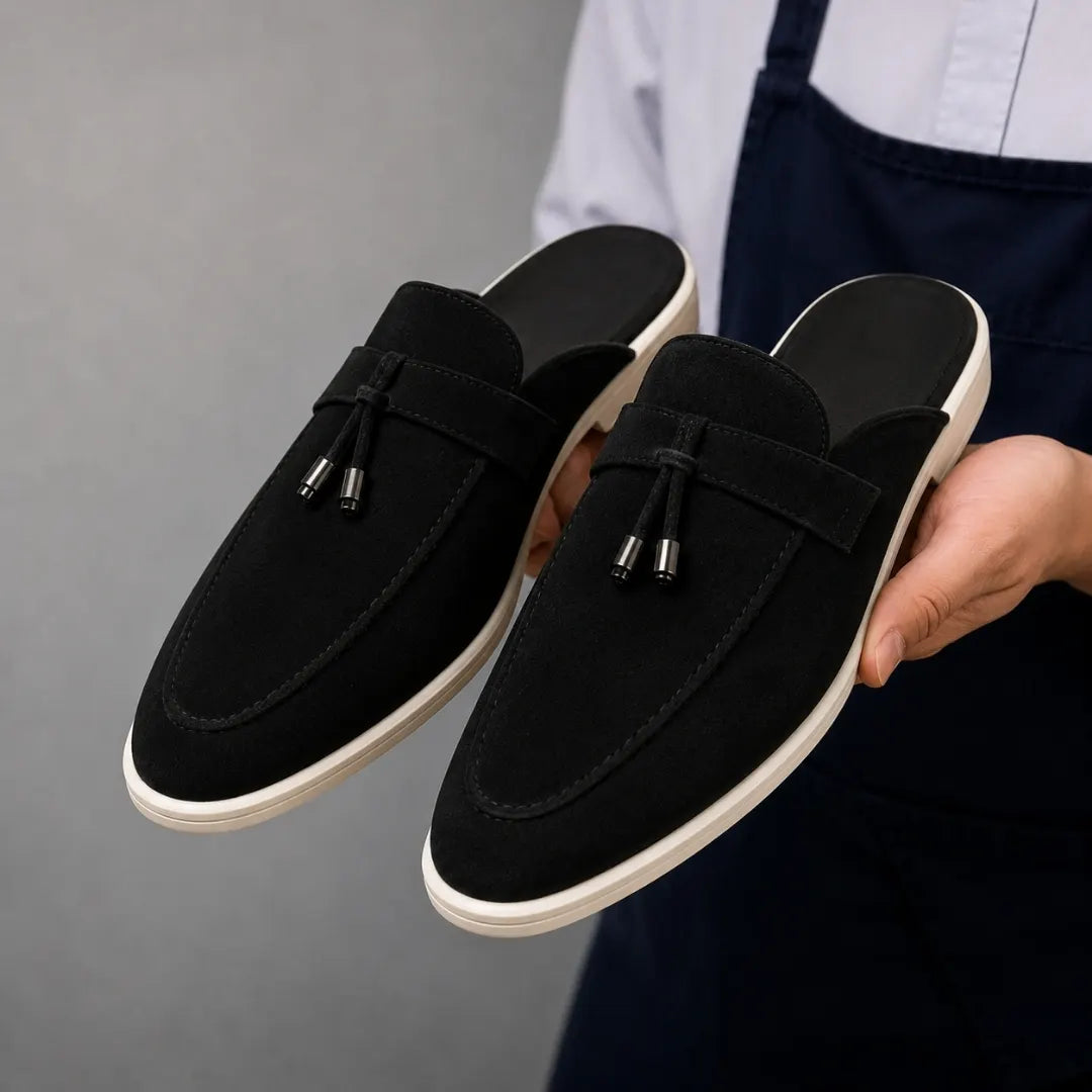 Man holding a pair of Melodiapelle Millo Mule shoes in black suede, close-up