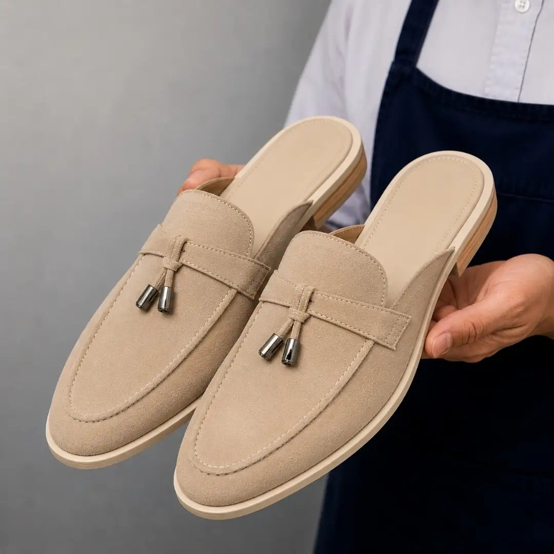 Man holding a pair of Melodiapelle Millo Mule shoes in sand beige suede, close-up
