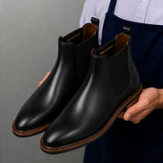 Man holding a pair of Melodiapelle Mirage Chelsea Boots in nero black leather, close-up