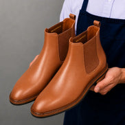 Man holding a pair of Melodiapelle Mirage Chelsea Boots in tan leather, close-up