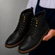 Man holding a pair of Melodiapelle Miranda Cap Toe Heritage Boots in black leather, close-up
