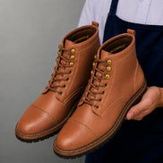 Man holding a pair of Melodiapelle Miranda Cap Toe Heritage Boots in tan leather, close-up