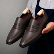 Man holding a pair of Melodiapelle Mirasol Two-Tone Dress Loafer shoes in brown leather, close-up