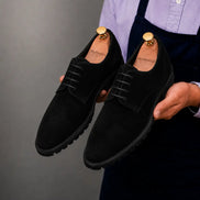 Man holding a pair of Melodiapelle Mission Classic Derby shoes in black suede, close-up