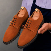 Man holding a pair of Melodiapelle Mission Classic Derby shoes in rust tan suede, close-up