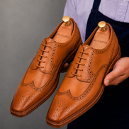 Man holding a pair of Melodiapelle Missourie Longwing Brogue Derby shoes in natural tan leather, close-up
