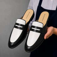 Man holding a pair of Melodiapelle Modena Mule shoes in black and white leather, close-up