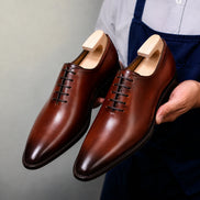 Man holding a pair of Melodiapelle Modesto Wholecut Oxford shoes in cognac tan leather, close-up