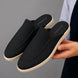 Man holding a pair of Melodiapelle Mole Mule shoes in black suede, close-up
