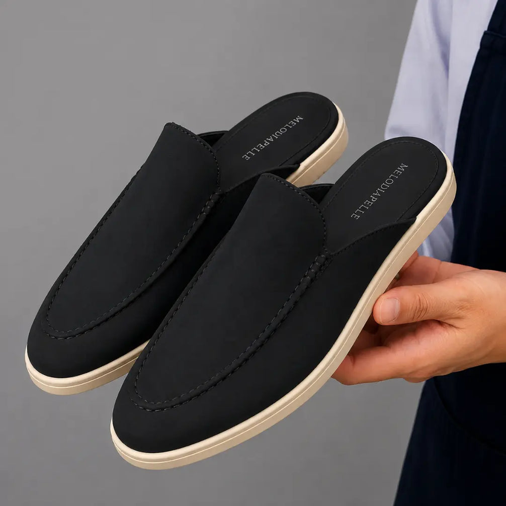 Man holding a pair of Melodiapelle Mole Mule shoes in black suede, close-up