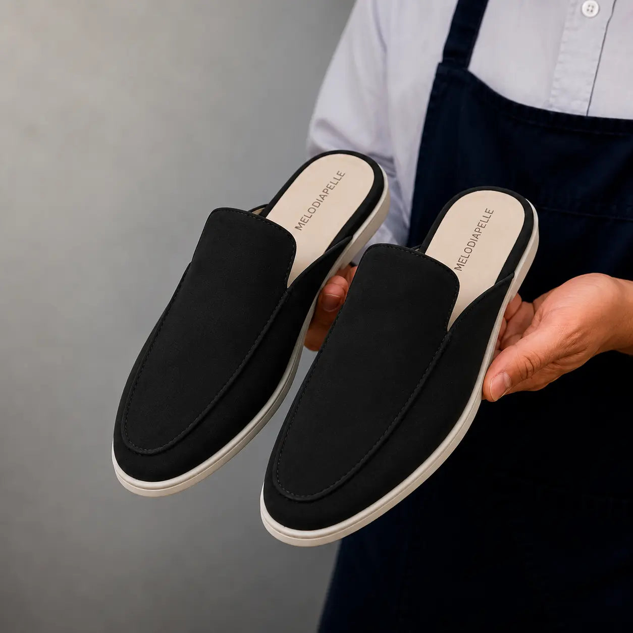 Man holding a pair of Melodiapelle Mole Mule shoes in black suede, close-up