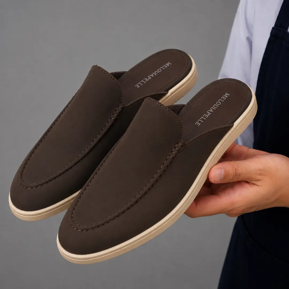Man holding a pair of Melodiapelle Mole Mule shoes in dark brown suede, close-up